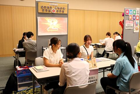 タブレットの画面を見ながら法人のブースで話を聞く学生